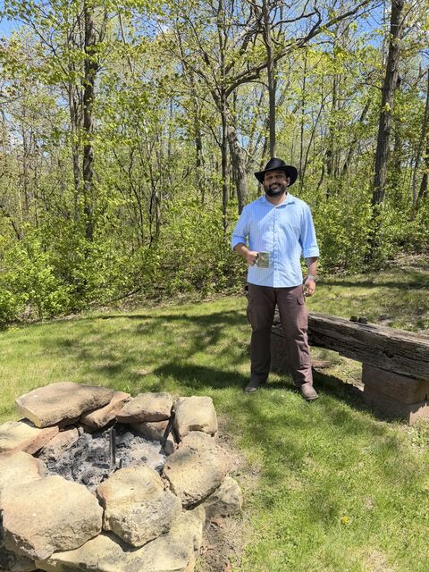 Tanmay beside a stone fire pit at a wooded campsite